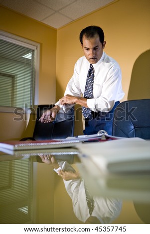 Middle-aged Hispanic businessman working in office rolling up sleeves looking down at paperwork