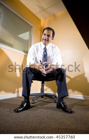 Middle-aged Hispanic businessman sitting on office chair in boardroom