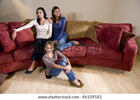 Indian mother and two mixed-race daughters sitting together at home in living room