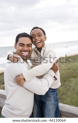 Happy African-American father and ten year old son laughing at beach