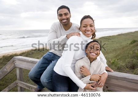Happy African-American parents with ten year old boy smiling and hugging at beach