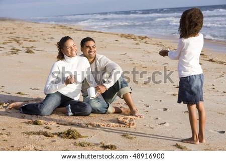 Six year old African-American girl gathering shells with parents on beach