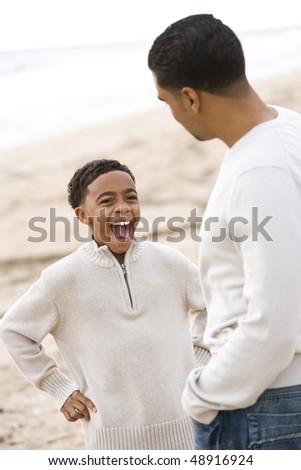 African-American father and ten year old son playing on beach, boy shouting