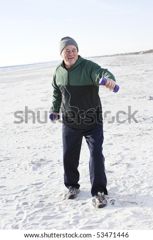 Senior man exercising with hand weights on beach listening to music