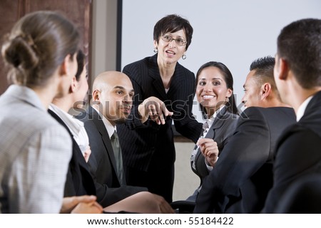 Diverse group of businesspeople conversing with woman standing at front