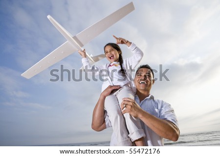 Hispanic dad and 9 year old child playing at beach with model plane