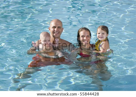 Portrait of young family with baby and toddler smiling in swimming pool
