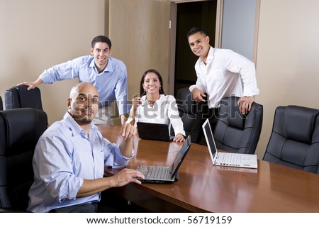 Mid-adult Hispanic office workers in boardroom meeting with laptops
