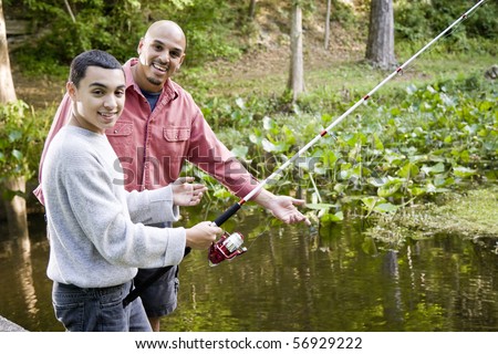 Hispanic 14 year old teen boy and father fishing in pond