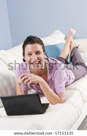 Woman relaxing at home on sofa with laptop surfing the internet