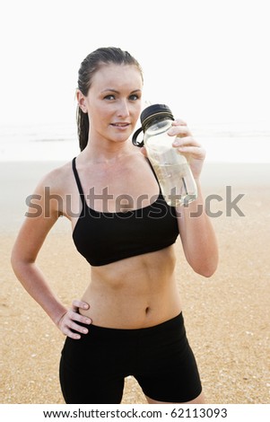 Front view of healthy fit young woman on beach drinking water