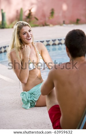 Young adult woman laughing and flirting with man sitting by swimming pool