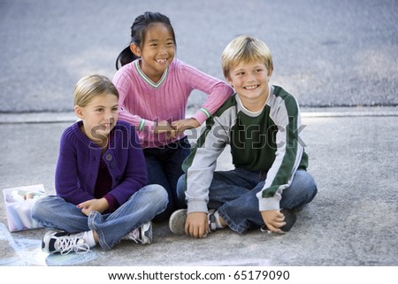 Three kids sitting on driveway smiling.  Ages 7 to 9