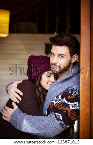 Young couple in a cabin in romantic scape in winter, She is leaning on his chest