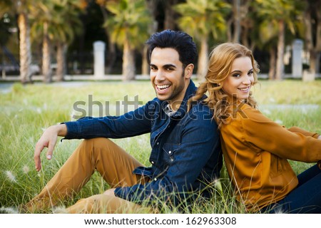 Fashion couple sitting in a grass field back to back