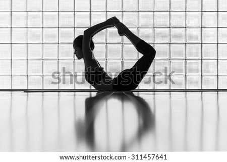 Young woman practicing in a yoga studio. This pose is called bow pose or dhanurasana.