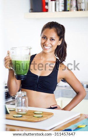 Woman preparing a green detox juice at home wearing sport clothes.
