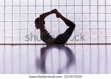 Young woman practicing in a yoga studio. This pose is called bow pose or dhanurasana.
