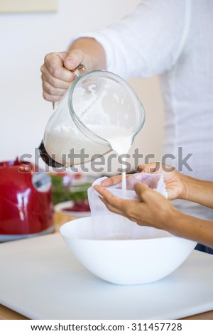 Couple preparing almond milk at home. Pouring the milk into a cheese cloth to filter it.