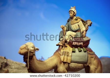 Older wise king with dromedary against blue sky.