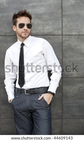 Young handsome man standing against wall with sun glasses and necktie