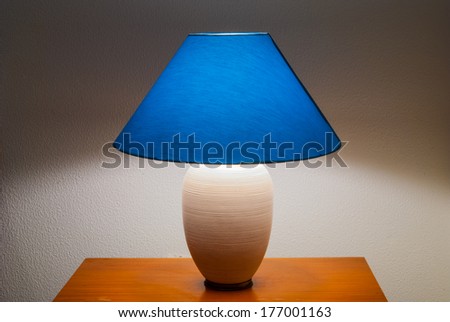 Lamp on a nightstand with a blue glow on a textured wall-diffused lighting