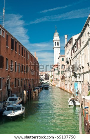 A picturesque view down a boat-lined canal in Venice, Italy with a leaning bell tower in the background