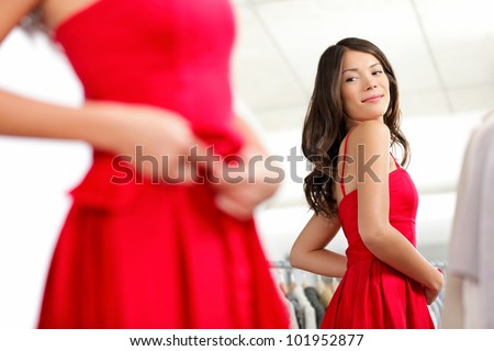 Girl trying dress in looking in mirror cheerful and happy. Cute beautiful mixed race Asian / Caucasian young woman in red dress.