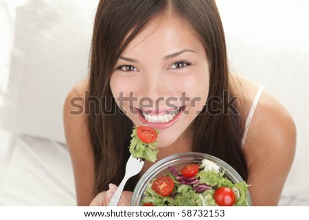 Woman eating salad. Portrait of beautiful smiling and happy mixed Asian Caucasian woman enjoying a healthy salad and cherry tomatoes snack.