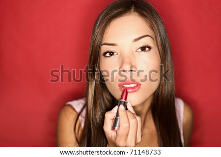 Woman putting red lipstick looking in mirror. Makeup at night getting ready before going to party.