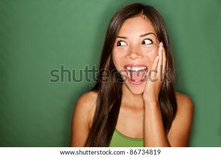 amazement - woman excited looking to the side. Surprised happy young woman looking sideways in excitement. Mixed race Chinese Asian / white Caucasian female model on green background.