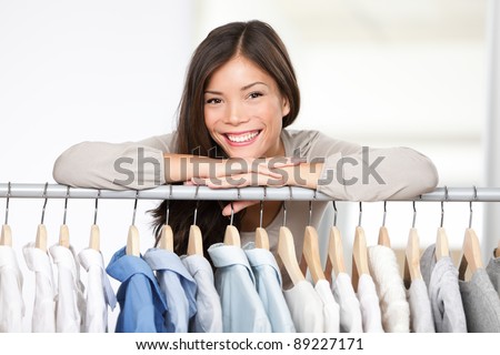 Business owner - clothes store. Young female business owner in her shop behind clothes rack smiling proud and happy. Multicultural Caucasian / Asian female model.