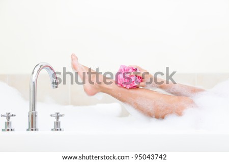 Woman in bath washing leg in bathtub with a lot of bubble bath foam. Leg of beautiful young woman in bath in bathroom.