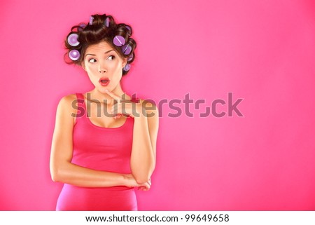 Funny beauty woman with hair rollers looking thinking to the side. Beautiful girl in pink on pink background. Multiracial Caucasian / Asian Chinese female hair model.