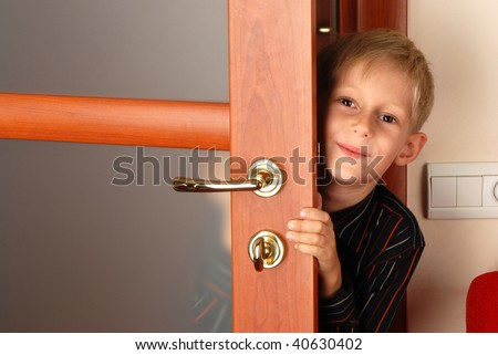 Joyful boy peeping out from behind door