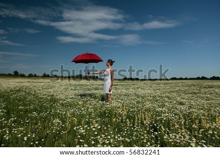 Woman in bright dress with red umbrella on meadow