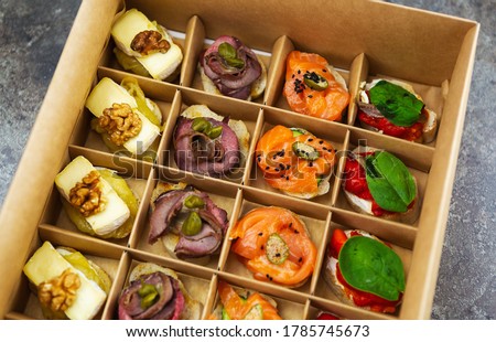 Catering food delivery in cardboard box for wine party.Delicious snacks delivered on venue in package for public event.Red fish fillet,veal meat,capers,brie cheese on canape bread for lunch meal Photo stock © 