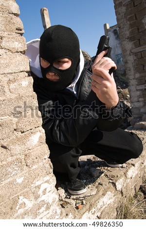 Criminal in black balaclava mask waiting for a victim round the corner