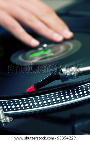 Focus is on the needle and the hand of a disc jockey is on the background