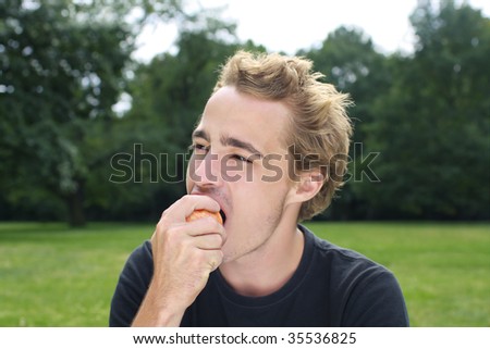young man eating apple in the park