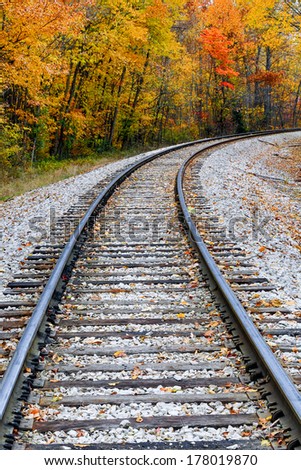 Railroad tracks curve through a landscape full of colorful fall foliage.