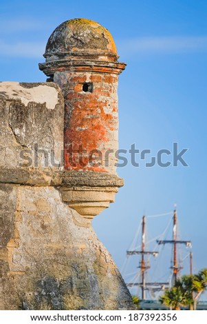 A round corner sentry box, on an old St. Augustine, Florida Spanish coquina stone fort called the Castillo de San Marcos, is backed by the tall masts of a Spanish Galleon in Matanzas Bay.