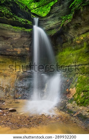 A seasonal waterfall flows over a rocky cliff into the Devil\'s Punchbowl in Indiana\'s scenic Shades State Park.
