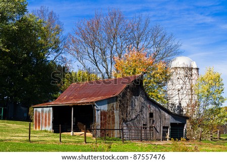 Small, old, rustic barn with a white silo and fall foliage and deep blue sky with wispy clouds.