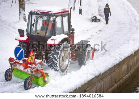Red tractor with scoop and automated brush removes snow on embankment in park. Tractor with snowplough and rotating brush sweeping snow from sidewalk. Municipal road sweeping vehicle with plow Photo stock © 