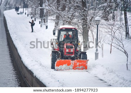 Snow removal tractor with rotating brush sweeping snow from footpath on embankment in park. Red tractor with scoop and automated brush removes snow. Municipal road sweeping vehicle with plow Photo stock © 