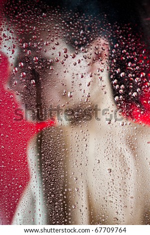 Beautiful slim girl behind wet glass