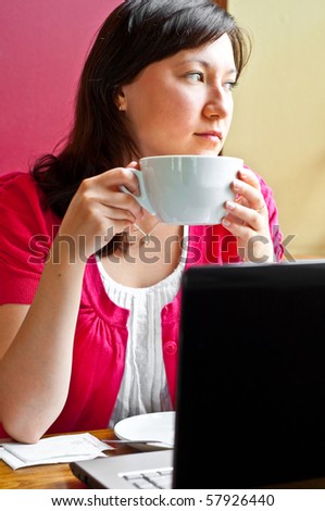 young woman drinking cappuccino and using laptop, distracted and looking out the window