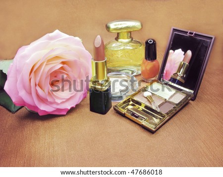 brown lipstick powder yellow rose eye shadow and perfume on satin cloth background