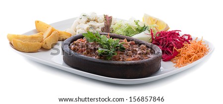 Beef casserole on a terracotta plate with salad and pasta on the side isolated on white background